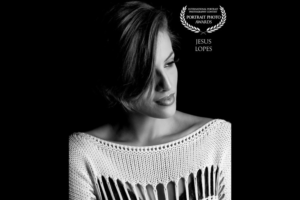 Retrato em preto e branco de mulher com blusa de tricô branca. Inclui selo do Portrait Photo Awards e autoria de Jesus Lopes
