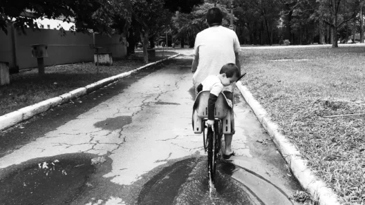 Homem e criança em uma bicicleta passando por uma poça d'água em um caminho arborizado