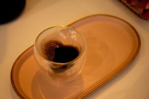 Xícara de vidro com café em formato de coração sobre uma bandeja oval rosa