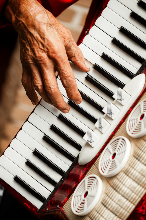 Mão de uma pessoa idosa tocando as teclas de um acordeão vermelho