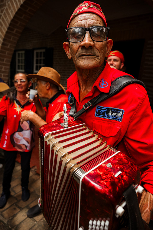 Homem idoso de óculos e traje vermelho tocando uma sanfona vermelha em um evento cultural