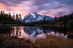 Montanha nevada refletida em um lago calmo sob um céu de tons rosa e roxo ao entardecer
