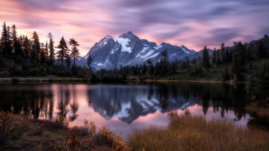 Montanha nevada refletida em um lago calmo sob um céu de tons rosa e roxo ao entardecer