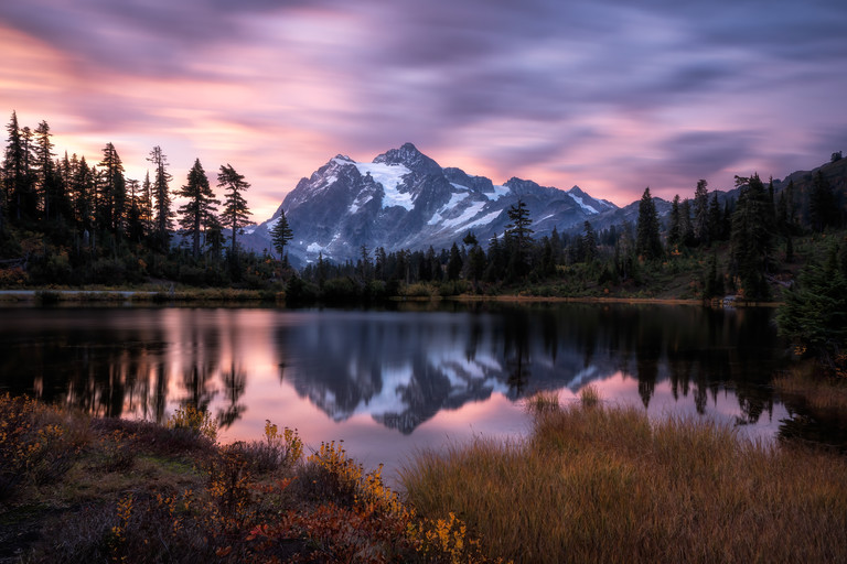 Montanha nevada refletida em um lago calmo sob um céu de tons rosa e roxo ao entardecer