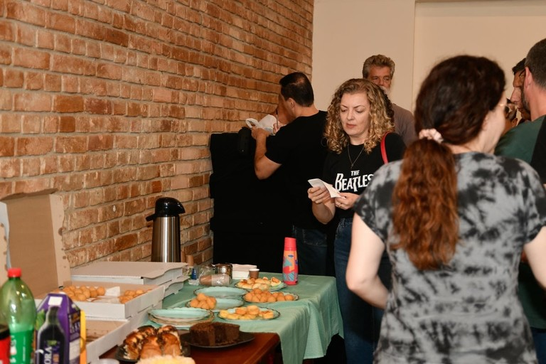 Pessoas reunidas em torno de uma mesa com lanches e café durante um evento social