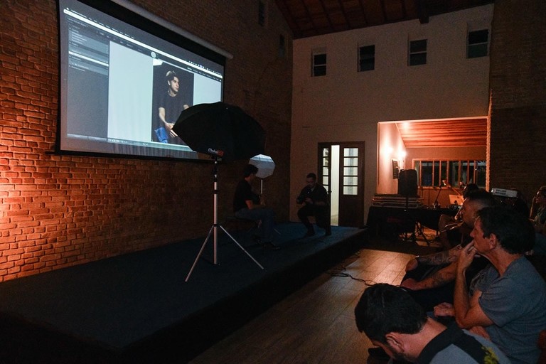 Workshop de fotografia com instrutor no palco, equipamento de iluminação e tela projetando a imagem para o público