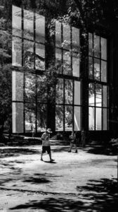 Fotografia em preto e branco com dupla exposição, sobrepondo grandes janelas a pessoas caminhando em um parque arborizado