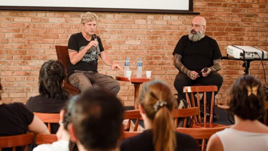 Dois homens conversam em um palco diante de uma plateia. Um deles fala ao microfone
