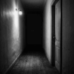 Corredor escuro e sombrio em preto e branco, iluminado por uma única lâmpada de parede ao lado de uma porta fechada